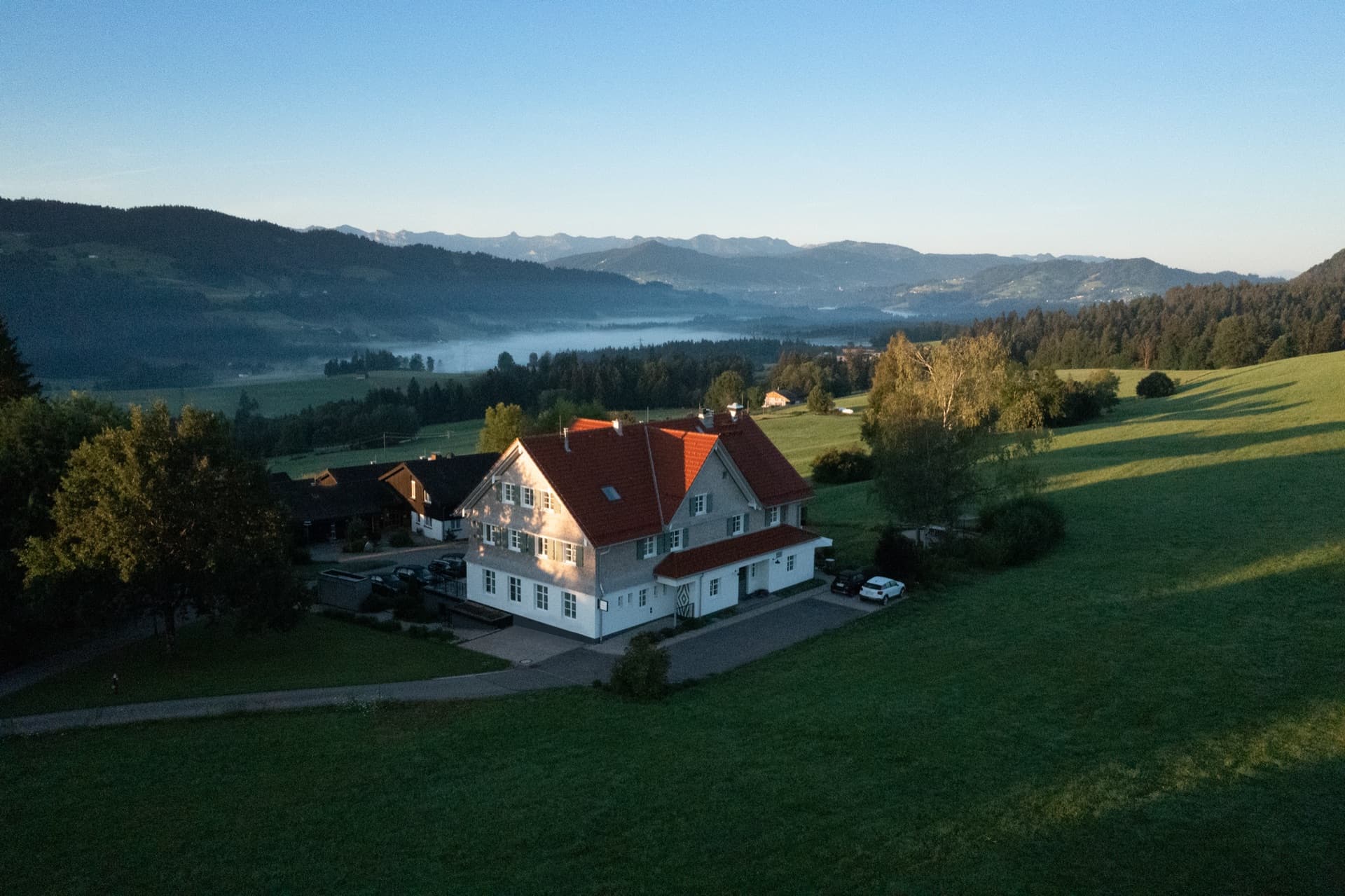 Luftaufnahme des Anwesens im Grünen, umgeben von Wiesen und Alpenpanorama